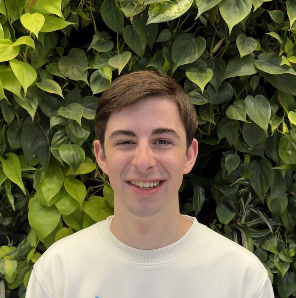 Portrait of Drake Jordan smiling in front of green foliage.